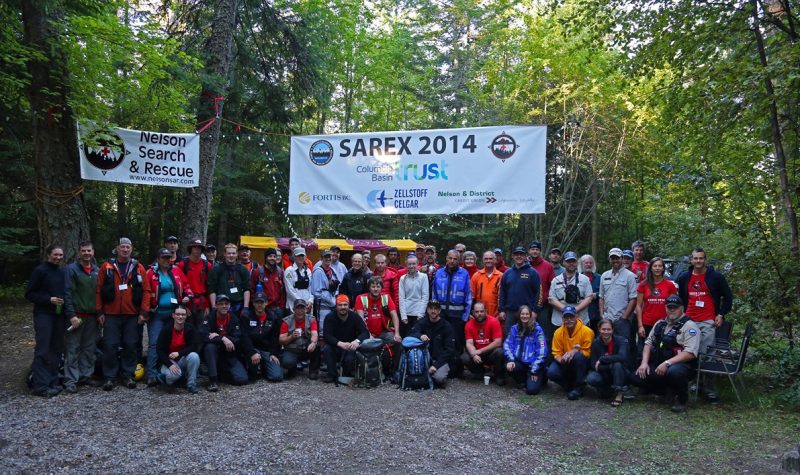A group of people gathered in the woods. Trees and SAREX banners behind.