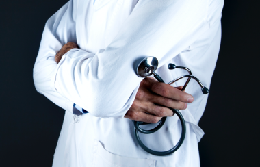 mid torso picture of a person wearing a white lab coat and holding a stethoscope in their hand