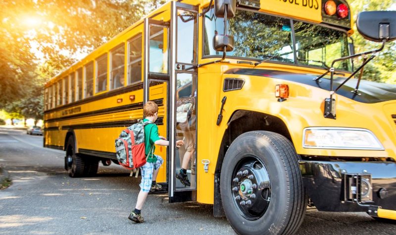 A child with a backpack boards a large yellow school bus.