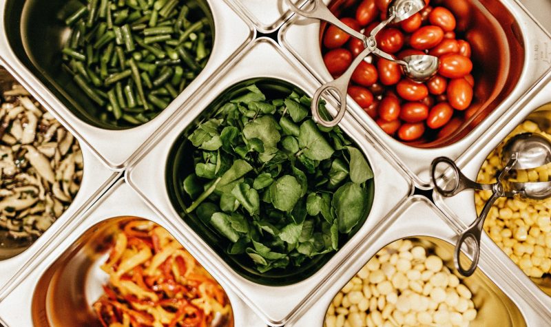 Stainless steel containers separate different foods such as spinach and tomatoes, beans and nuts for a buffet style serving platter.