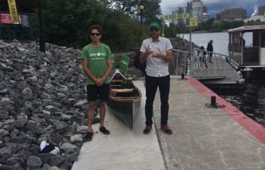 Pontiac Green candidate Shaughn McArthur, wearing a green t-shirt and Hull-Aylmer candidate Simon Gnocchini-Messier stand in front of a canoe on a dock next to the Ottawa River.