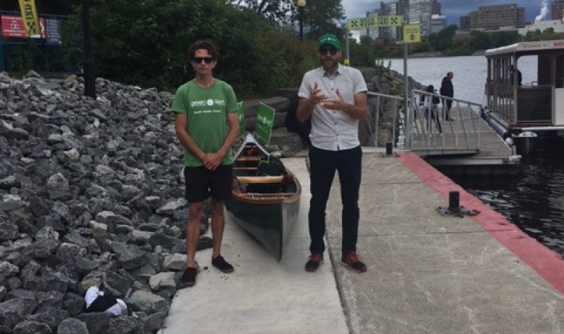 Pontiac Green candidate Shaughn McArthur, wearing a green t-shirt and Hull-Aylmer candidate Simon Gnocchini-Messier stand in front of a canoe on a dock next to the Ottawa River.