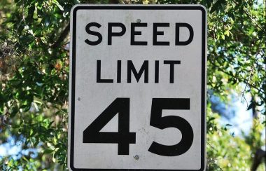 On aperçoit un panneau blanc de limite de vitesse avec l'inscription en anglais « speed limit 45 ». En arrière plan, les arbres et la verdure laisse deviner un quartier résidentiel.