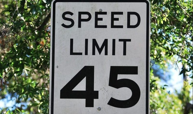 On aperçoit un panneau blanc de limite de vitesse avec l'inscription en anglais « speed limit 45 ». En arrière plan, les arbres et la verdure laisse deviner un quartier résidentiel.