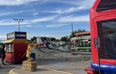 Fairground equipment including a bouncy castle, coupons vendor, and fair rides set up in a parking lot.