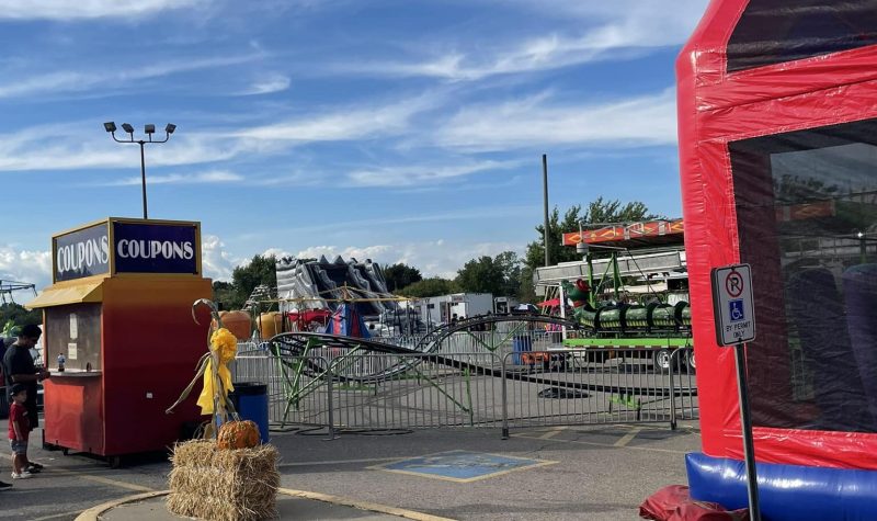 Fairground equipment including a bouncy castle, coupons vendor, and fair rides set up in a parking lot.