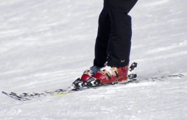 Une personne portant des botte de ski alpin rouge et des pantalons à neige noir dévale une pente. On voit seulement les skis, ses bottes et le pantalon à neige jusqu'au genou de la personne.