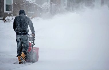 Un homme déneige sa cours avec sa souffleuse à neige.
