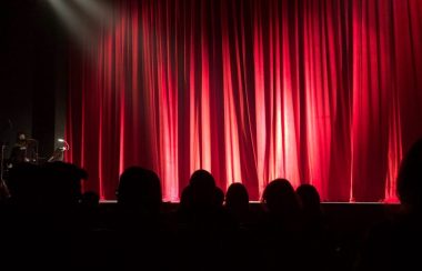 Une foule devant un grand rideau rouge dans une salle de spectacle