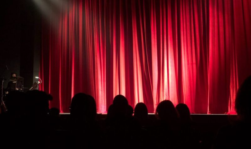 Une foule devant un grand rideau rouge dans une salle de spectacle