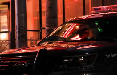 On peut voir une auto-patrouille noire dans une rue urbaine. La photo a été prise en soirée et on peut voir le reflet des lumières de la ville sur la voiture.