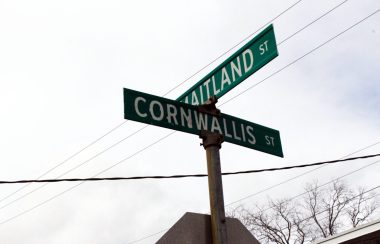 Le panneau des rues au croisement de la rue Cornwallis et Saltland. Photo prise vers le ciel, on voit des cable électrique et du ciel gris.