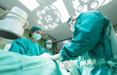 A medical team in green scrubs in an white operating theatre in a hospital
