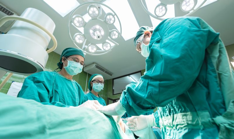 A medical team in green scrubs in an white operating theatre in a hospital