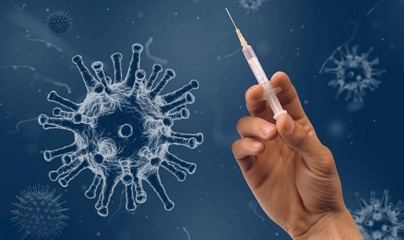 Une main tient une seringue de vaccin devant un logo de coronavirus