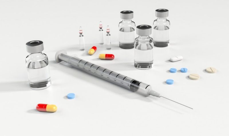A photo of a needle and various prescription pills are shown.