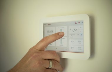 A hand can be seen adjusting temperatures on a thermostat positioned on a wall.
