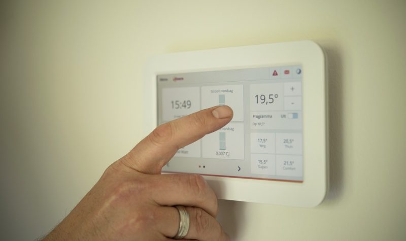 A hand can be seen adjusting temperatures on a thermostat positioned on a wall.