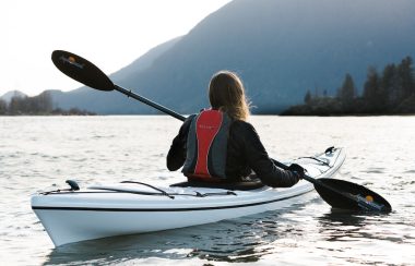 woman in red and black vest riding a kayak in daytime