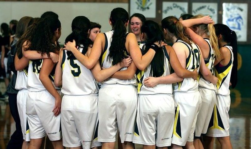 Équipe de basketball féminine. Le maillot de l'équipe en caucus sont blancs avec une ligne jaune entouré de deux lignes vertes.