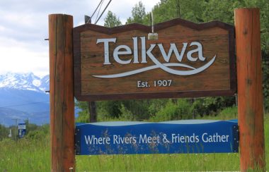 A wooden sign is beside a highway and it reads Telkwa: Where Rivers Meet and Friends Gather