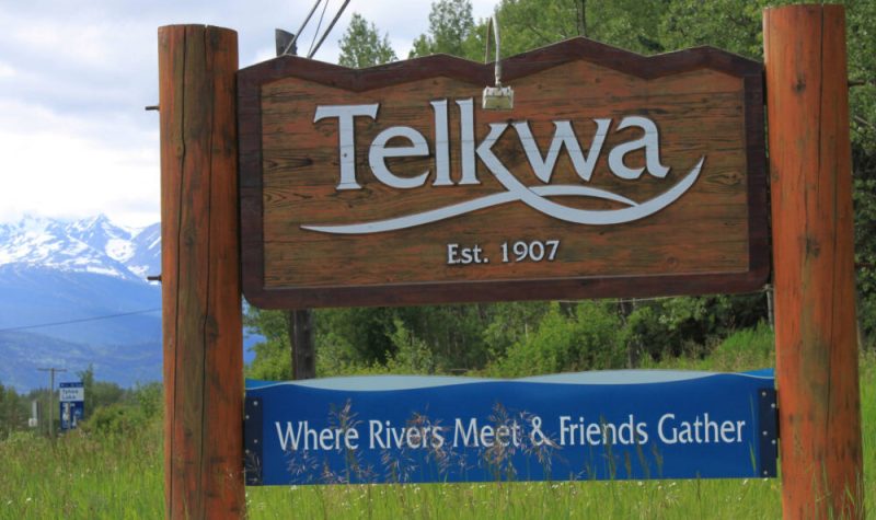A wooden sign is beside a highway and it reads Telkwa: Where Rivers Meet and Friends Gather