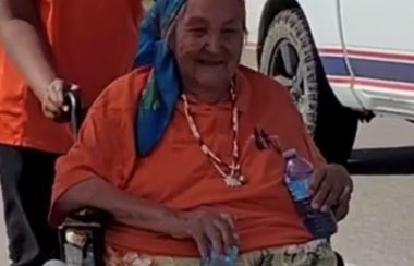 Elder wearing an orange shirt sits in a wheelchair outside