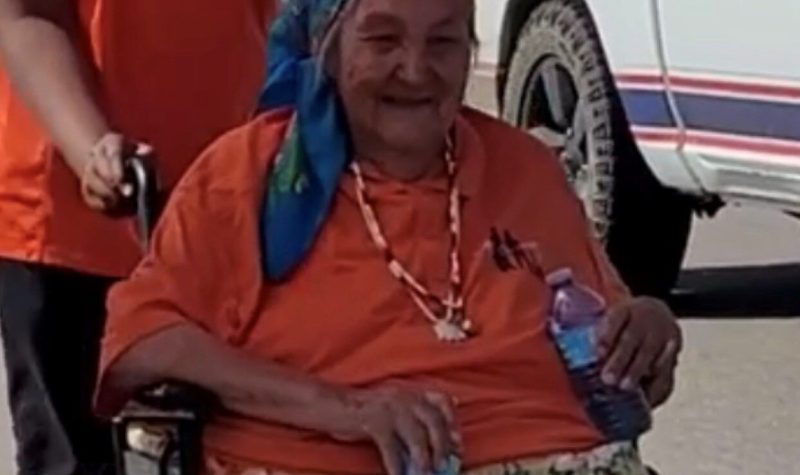 Elder wearing an orange shirt sits in a wheelchair outside