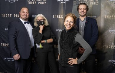 A group shot of some attendees at Theatre Lac-Brome and Amazon's launch of the Three Pines series. They are standing behind a black backdrop with Three Pines and Prime Video written all over it.