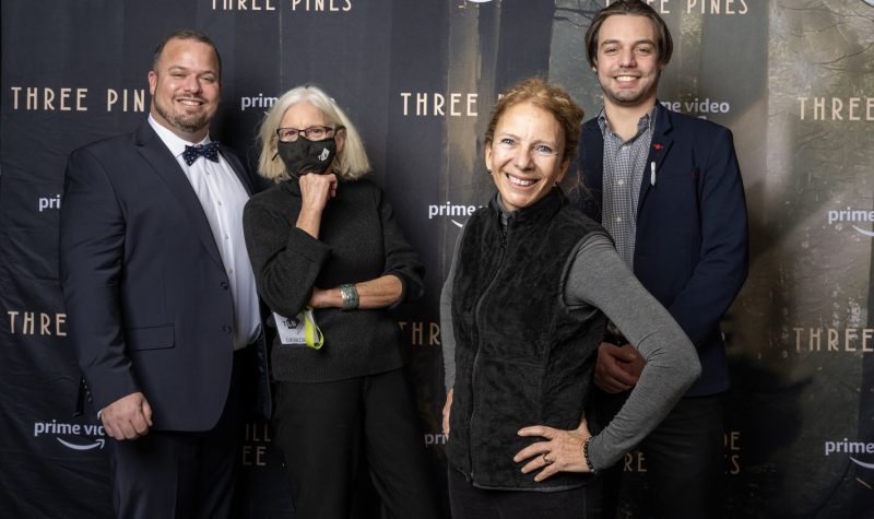A group shot of some attendees at Theatre Lac-Brome and Amazon's launch of the Three Pines series. They are standing behind a black backdrop with Three Pines and Prime Video written all over it.