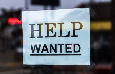 A printed sign in a window says HELP WANTED in capital letters