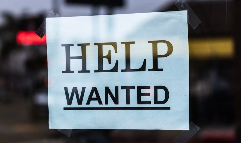 A printed sign in a window says HELP WANTED in capital letters