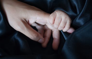 Une main d'enfant tient une main de parent, les deux porte des manche de couleur sombre