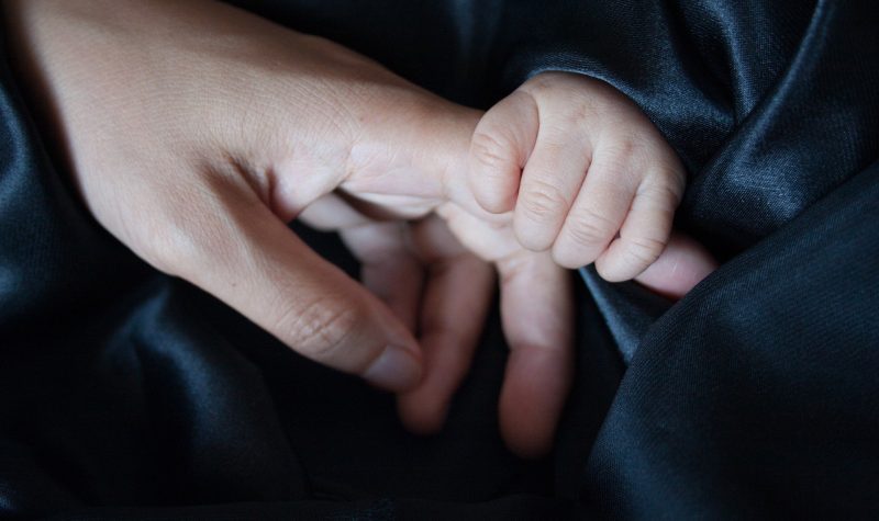 Une main d'enfant tient une main de parent, les deux porte des manche de couleur sombre