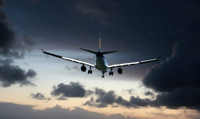 Avion qui plane dans le ciel, sur fond d'ambiance crépusculaire couvert en partie de sombres nuages.