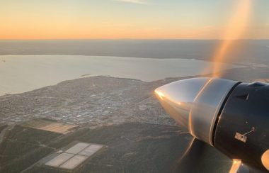 L'hélice d'un avion tourne dans le ciel avec en arrière plan la ville de Sept-Îles.