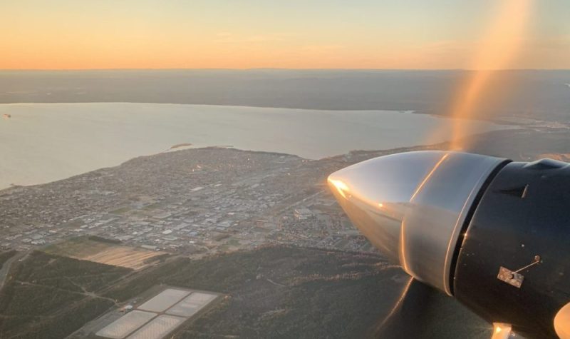 L'hélice d'un avion tourne dans le ciel avec en arrière plan la ville de Sept-Îles.