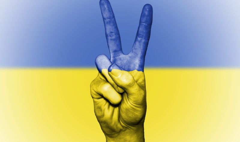 Le symbole de la paix en forme de V fait avec la main avec le drapeau Ukrainien en arrière fond.