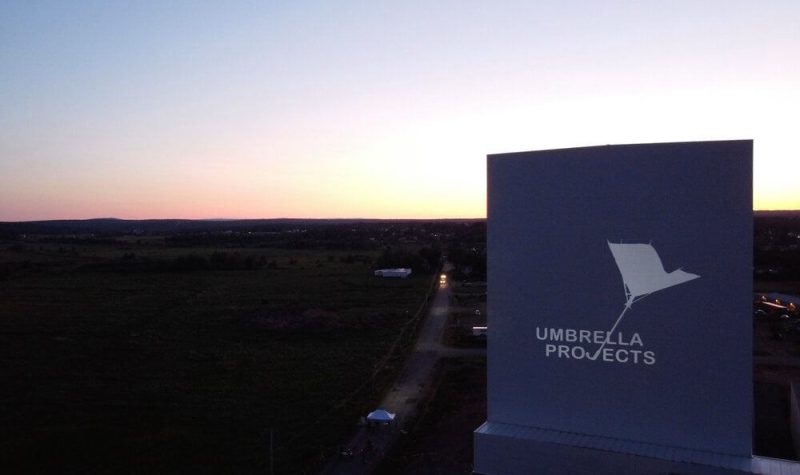 The Umbrella Projects logo is projected onto a tall outdoor building at dusk.