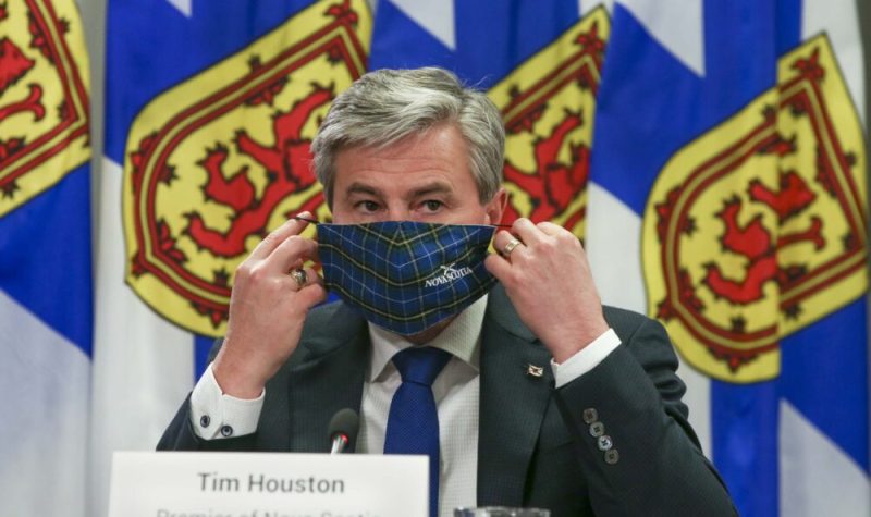 Homme portant un masque assis à une table avec des drapeaux de la Nouvelle-Écosse en arrière plan.