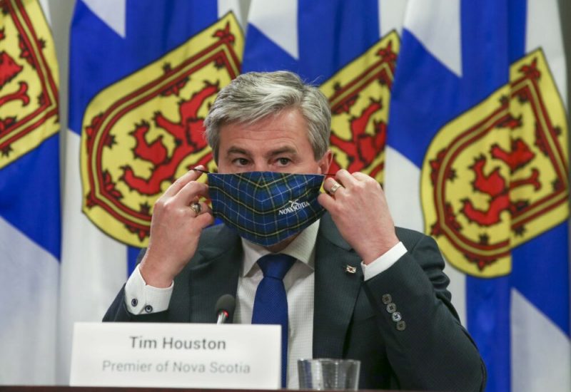 Homme portant un masque assis à une table avec des drapeaux de la Nouvelle-Écosse en arrière plan.