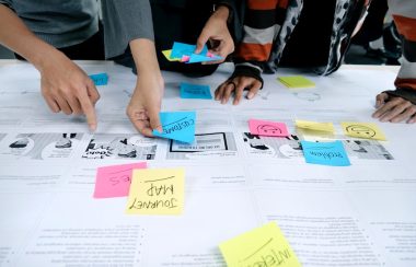 People's hands are moving around colourful sticky notes on a large piece of paper