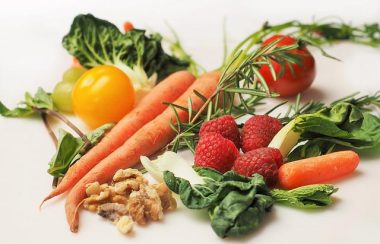Image de plusieurs fruits et légumes. On retrouve deux carottes, une carotte biologique, quatre framboises, une tomate rouge, une tomate jaune, des feuilles vertes et des noix de Grenoble.