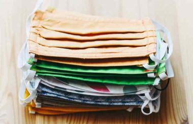 A pile of multicoloured cloth masks sits on a wooden surface.