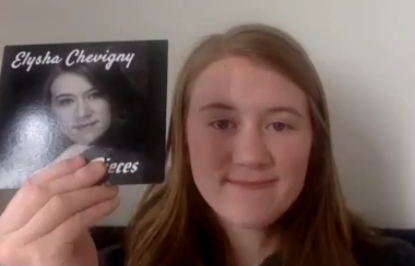Elysha Chevigny tient une copie physique de son album en souriant à la caméra.