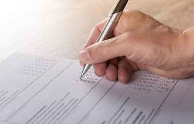 La main d'une personne votant sur un papier à l'aide d'une plume grise