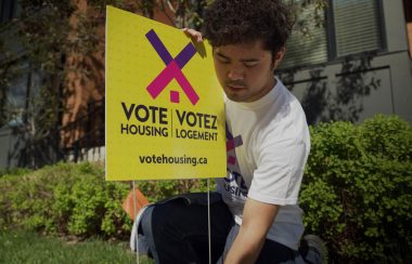 A volunteer install a Vote Housing Campaign sign on a lawn