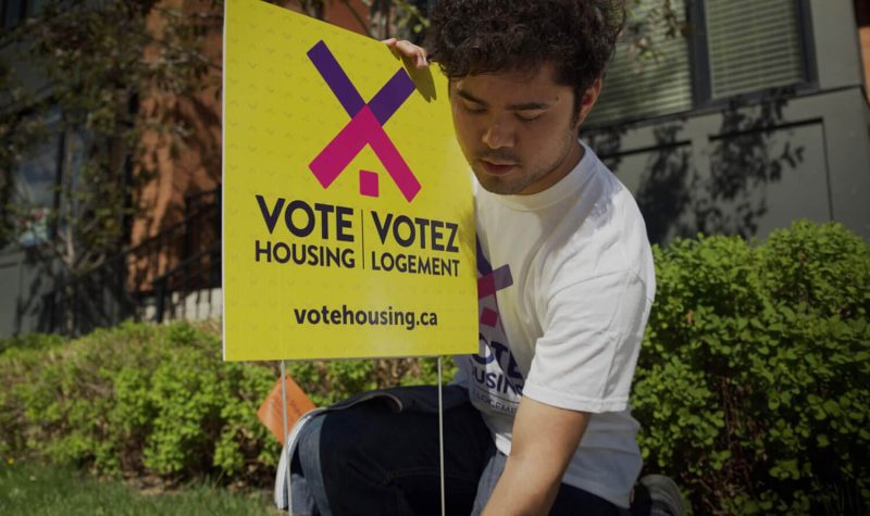 A volunteer install a Vote Housing Campaign sign on a lawn