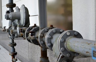 A grey water pipe is shown next to a building.