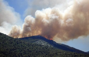 De la fumée monte dans le ciel derrière une montagne.